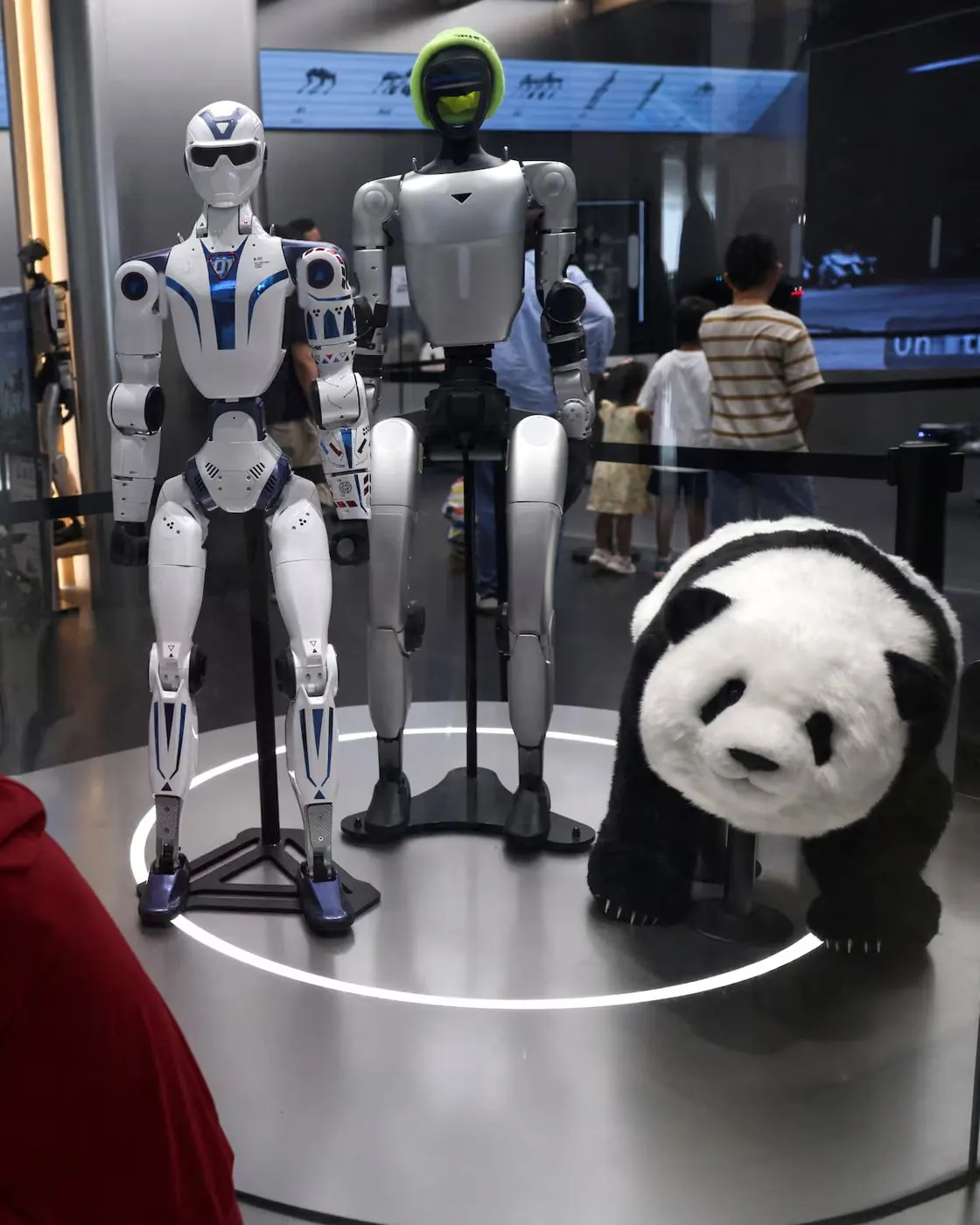 Humanoide R1, Humanoide G1 e Pooh Panda Robô lado a lado numa vitrine iluminada
